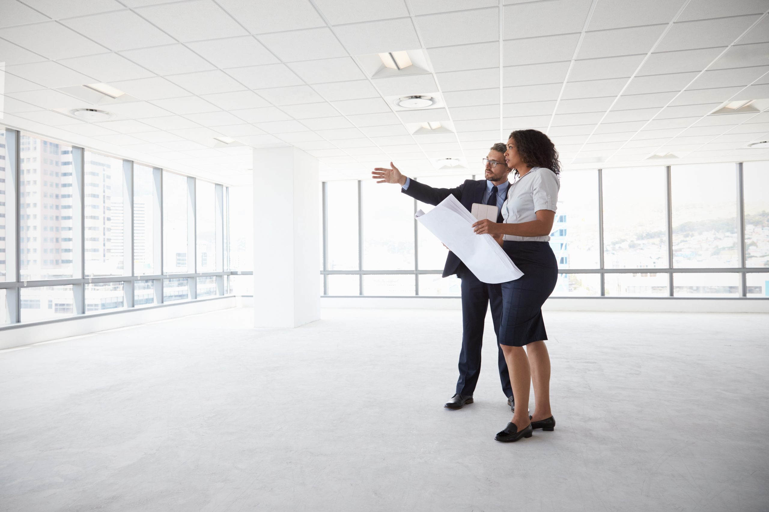 real estate agent helping commercial real estate buyers look at plans in an empty office